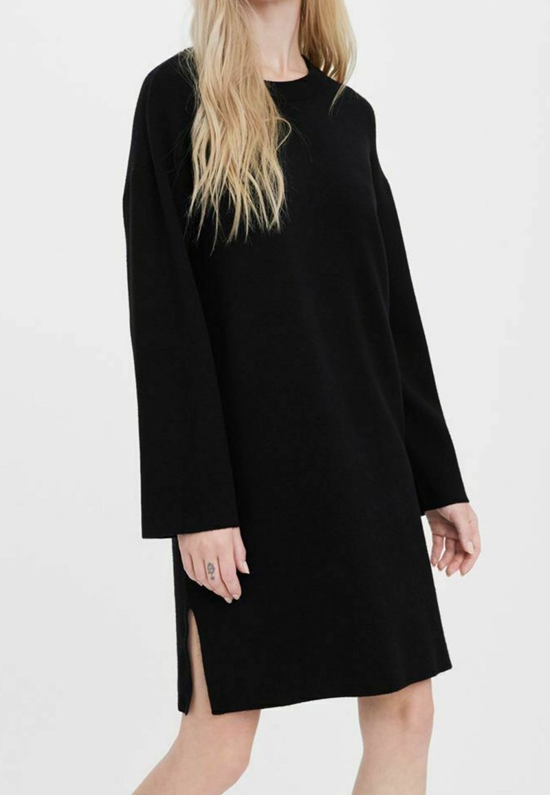 Svart stickad klänning med långa ärmar, rund halsringning, sidoflikar och avslappnad passform. Slät textur utan synliga mönster eller detaljer.