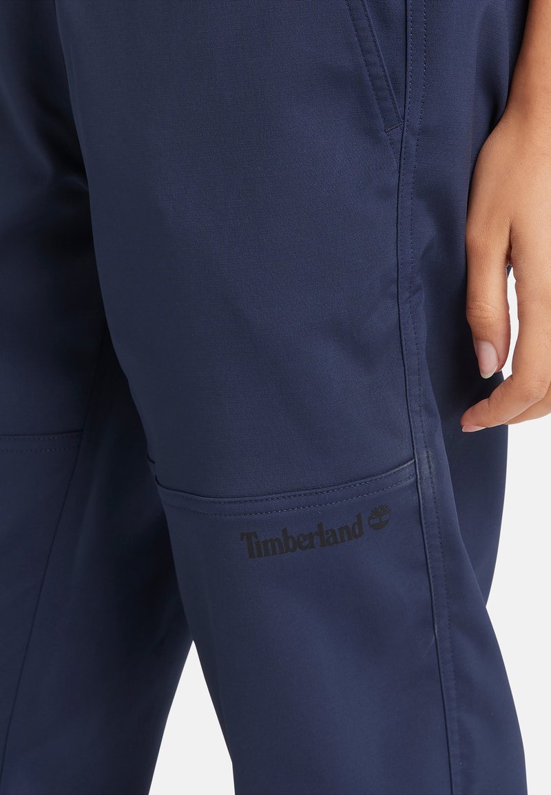 Pantalons bleu marine en tissu lisse avec une coupe droite. Présentent un logo Timberland noir sur le côté et des détails de couture horizontale.