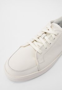 Baskets en cuir blanc avec lacets plats, bout arrondi et accents cousus. Texture lisse et design minimaliste.