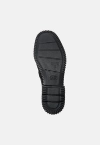 Suela de zapato de goma negra con un patrón estriado, que presenta una superficie texturizada y un logotipo de marca en relieve. Diseñada para la durabilidad y la tracción.