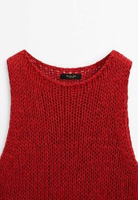 Haut rouge en tricot sans manches avec un large décolleté arrondi et une texture lâche. Étiquette intérieure indiquant "Maison D'Isle". Aucune décoration supplémentaire.