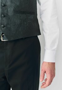 Fekete paisley mintás mellény gombokkal, fehér ing és fekete nadrág fölé öltözve. Simogatós anyag és testreszabott illeszkedés, oldalzsebből.