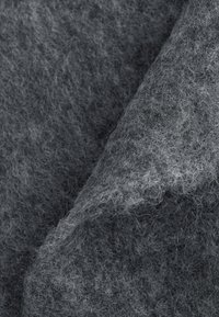 Nahaufnahme von weichem, grauem Filzstoff mit sichtbaren feinen Fasern und einem umgeschlagenen Rand, der subtile Schatten und Textur erzeugt.