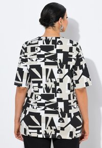 Camiseta gráfica en blanco y negro con un audaz patrón de letras abstractas sobre un fondo beige claro, mangas cortas y un cuello redondeado.