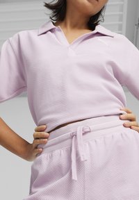 Jasnofioletowa koszulka polo z krótkim rękawem z fakturowanej tkaniny z kołnierzykiem, zestawiona z dopasowanymi spodniami z fakturowanego materiału z elastycznym paskiem na sznurku.