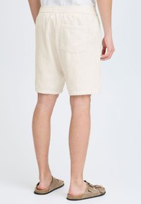 Beige kordfløyels-shorts med avslappet passform, elastisk midjebånd og en enkelt baklomme. Glatt tekstur med vertikal ribbestruktur.