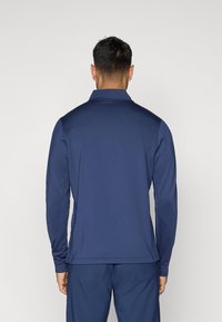 Πολό μπλούζα με μακριά μανίκια σε ναυτικό μπλε χρώμα με υφή στο ύφασμα. Διαθέτει γιακά και μανσέτες, καθώς και ευθεία άκρη.