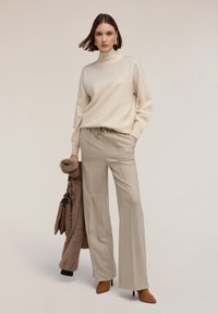 Krémový rolák spárovaný s širokými kalhotami s světle béžovým vzorem. Modelka nese hnědou kabelku a má na sobě texturovaný dlouhý kabát.