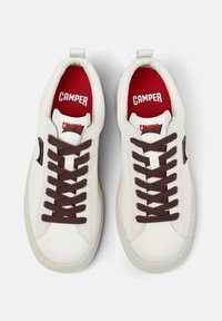 White Camper sneakers with brown laces and red inner soles, viewed from above, showing logo on tongue and inside sole.