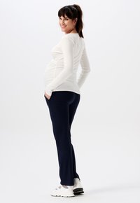 Lichtgewicht crème lange mouwen top gecombineerd met marineblauwe stretchbroek en witte sneakers. De top is aansluitend en benadrukt een zwangere silhouet.