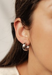 Orecchini a cerchio in metallo con una finitura argento lucida, caratterizzati da una superficie liscia e una forma rotonda, indossati sul lobo dell'orecchio.