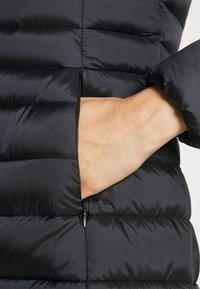 Sort pufferjakke med en lynlåslomme på siden, sydd mønster og glat, shiny stoftekstur.