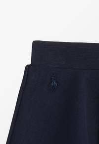 Námořnické modré kalhoty s texturovaným pasem. Obsahují vyšívané logo ve shodném odstínu. Materiál vykazuje jemný diagonální vzor.