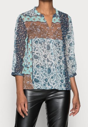 Kvinde iført en langærmet patchwork bluse med blomster- og dyreprint kombineret med sorte bukser i imiteret læder.