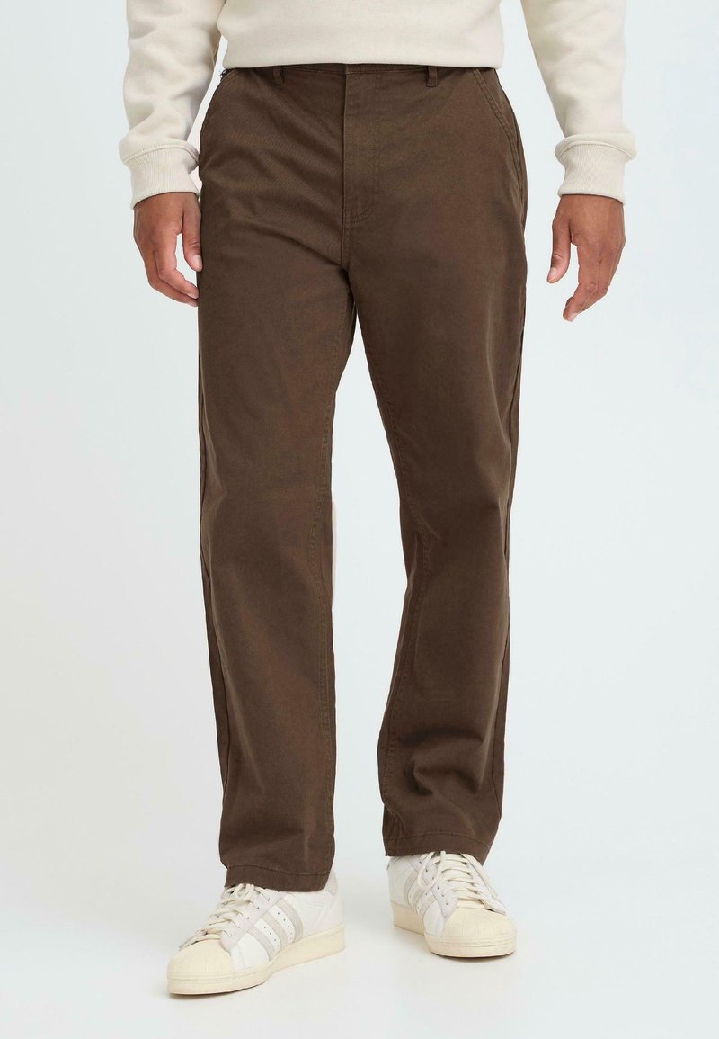 Brune, bomuldsblandede bukser med lige snit, der har frontlommer og en glat tekstur, båret sammen med hvide sneakers.