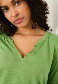 Green cotton short-sleeve shirt with a V-neck and six buttons, featuring a light, textured fabric and a relaxed fit.