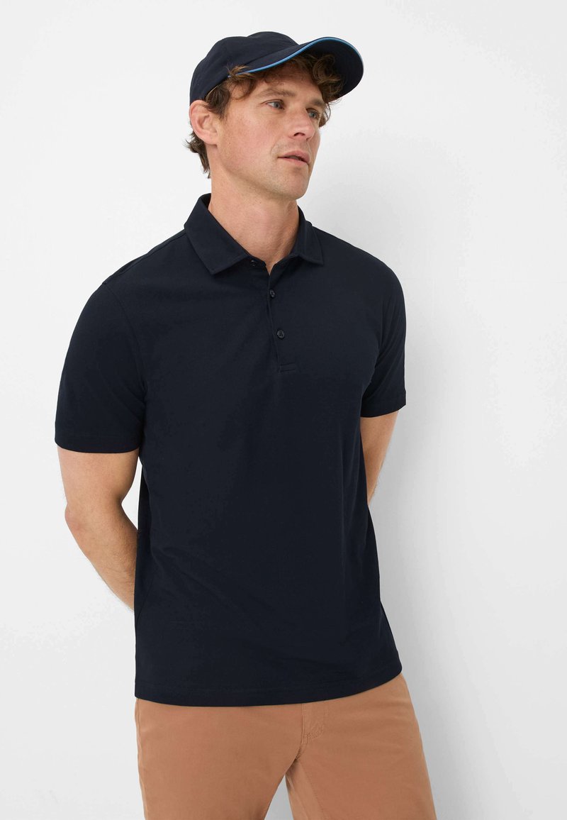 Navyblaues Polohemd mit kurzen Ärmeln und einer Drei-Knopf-Leiste. Kombiniert mit einer navyblauen Mütze mit einem blauen Akzent auf dem Schirm.