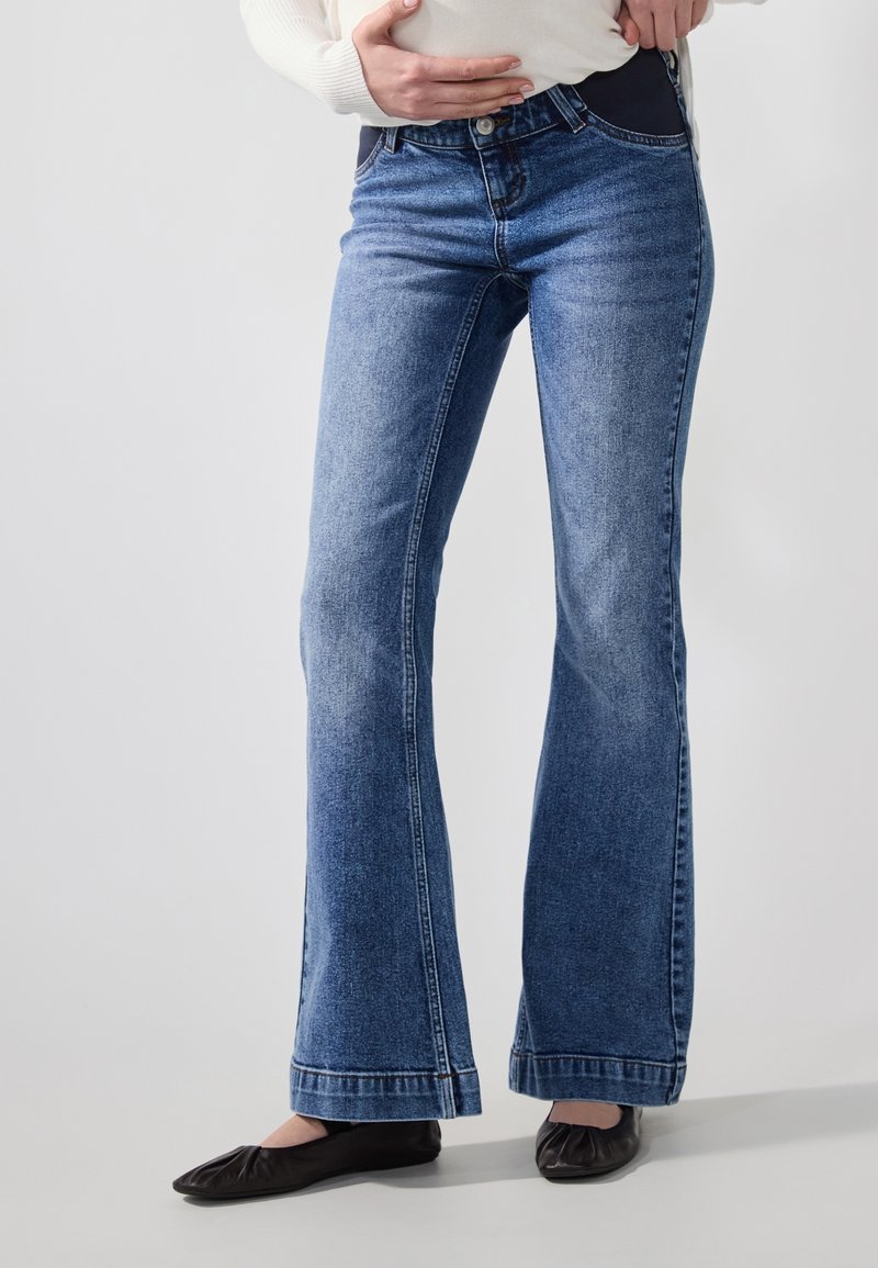 Jeans de denim azul acampanados con un lavado medio y un ligero desvanecimiento. Presentan un cierre de botón, bolsillos frontales y un ajuste entallado en la cintura.