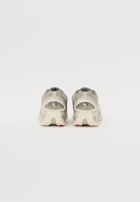 Szare buty sportowe z siateczkową cholewką, wyściełanym kołnierzem i wyraźnymi gumowymi podeszwami, z czerwonym akcentem na pięcie i widocznym logo.