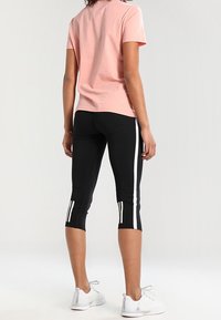 Różowy bawełniany t-shirt z krótkimi rękawami, zestawiony z czarnymi legginsami capri z białymi pionowymi paskami po bokach oraz białymi butami sportowymi.