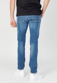Jeans de mezclilla azul con corte slim, que cuentan con bolsillos traseros bordados y una textura suave. Combinados con zapatillas blancas.