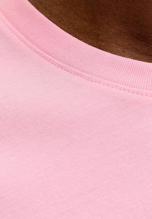 Približni prikaz tamne kože koja nosi rozu pamučnu majicu s okruglim izrezom, prikazujući teksturu tkanine i detalje šavova.