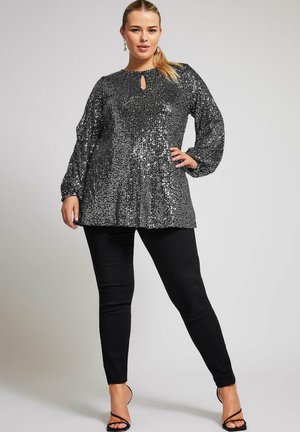 Top nero con paillettes, maniche lunghe e puffate, e scollatura a occhiello, abbinato a pantaloni neri slim e tacchi neri con cinturino.