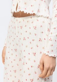 Gros plan sur une personne portant un pyjama en tissu côtelé blanc avec un petit imprimé floral rose, montrant le ventre et la main sur le côté.