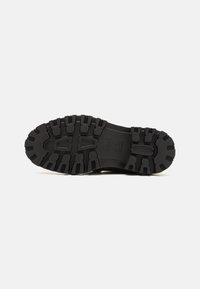 Black rubber sole with a rugged tread pattern, featuring deep grooves and raised accents for traction and durability.