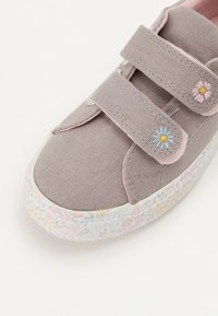 Baskets en toile grises avec des accents roses et deux bandes Velcro. Présente un motif floral sur la semelle et des fleurs brodées sur les côtés.