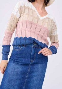 Femme portant un pull en tricot multicolore avec des rayures bleues, roses, beige et blanches, et une jupe en denim bleu taille haute.