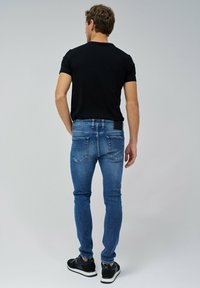 Jeans de denim azules ajustados con un ligero desvanecimiento, cinco bolsillos y pasadores para cinturón. Combinados con una camiseta negra de manga corta y zapatillas negras.