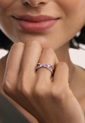 Anillo de oro rosa con un diseño retorcido, adornado con gemas rosas y transparentes, exhibido en una mano con tono de piel natural.