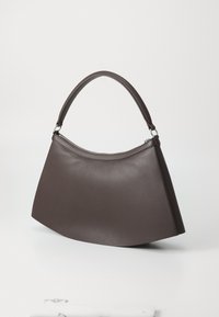 Sac à bandoulière en cuir brun foncé avec une silhouette courbée et une seule poignée rembourrée, doté d'une fermeture éclair sur le dessus, sur un fond uni.