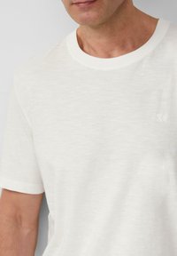 Witte T-shirt met korte mouwen, gemaakt van zachte, gestructureerde stof. Heeft een ronde halslijn en een subtiel logo op de linkerkant van de borst.