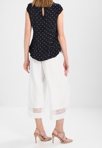 Blusa navy a pois con maniche corte, dettaglio chiave sul retro, abbinata a pantaloni bianchi a gamba larga con dettagli in pizzo all'orlo.
