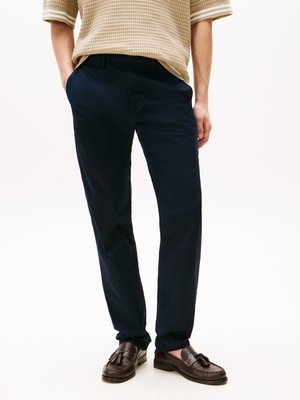 Navy blue cotton chinos with a smooth texture, slim fit, side pockets, and a button closure. Worn with brown loafers.