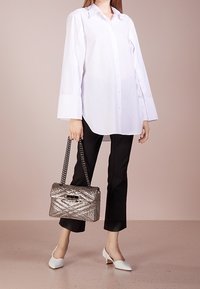 Camisa blanca de botones con mangas largas, pantalones negros ajustados y un bolso plateado brillante con correa de cadena, combinado con zapatos blancos de punta.