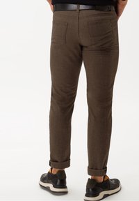 Brown slim-fit pants with a textured finish, featuring two back pockets and rolled cuffs. Paired with black and orange sneakers.