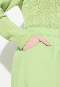 Hellgrüner Strickpullover mit einem strukturierten Kabelmuster und gerippten Bündchen, kombiniert mit passenden hoch-taillierten Hosen mit seitlichen Taschen.