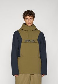 Giacca a cappuccio verde oliva e blu navy con tasca frontale e logo. Presenta una finitura testurizzata e una vestibilità comoda con maniche lunghe.