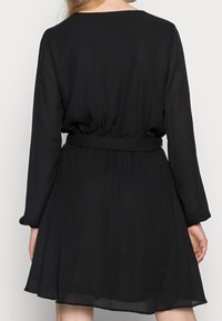Robe noire avec des manches longues, une taille ajustée et une jupe évasée. Fabriquée dans un tissu léger et semi-transparent avec une texture douce.