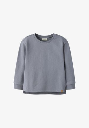 Langermet, lysegrå crewneck-genser med ribbede mansjetter og en liten brun merkelapp nær nederkanten på venstre side.