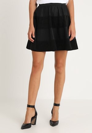 Falda negra acampanada con un diseño texturizado, que presenta paneles alternos de tela lisa y perforada. Combinada con zapatos de tacón altos negros.