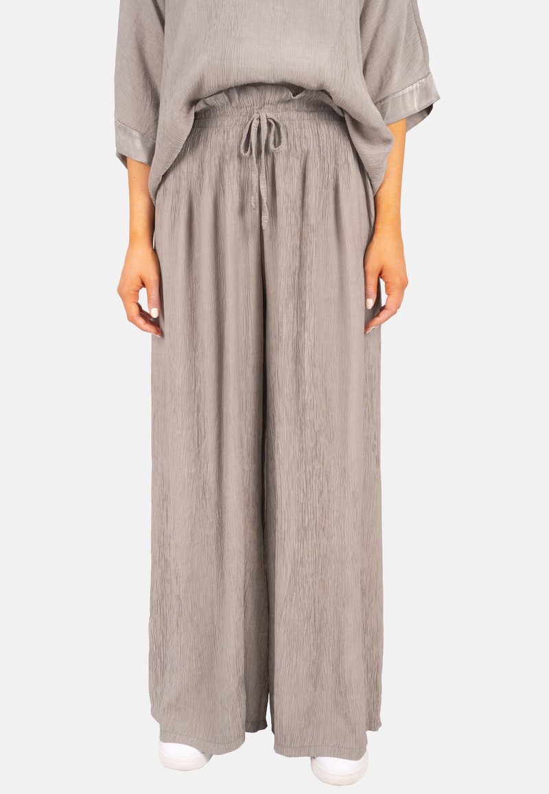 Pantalons larges plissés gris clair avec une taille élastique et un cordon de serrage. Présente un design fluide et une texture douce. Associés à des baskets blanches.