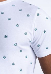 T-shirt alb cu un model repetat de mici valuri verzi și soare. Fabricat dintr-un material moale din bumbac, cu o croială ajustată.