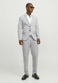 Light gray suit made of smooth material, with a single-breasted jacket, two pockets, and matching pants, worn with a white shirt and sunglasses.