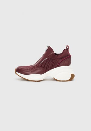 Scarpa sportiva bordeaux con pannelli in rete, chiusura con zip e suola bianca spessa. Presenta dettagli testurizzati e una linguetta per il tiraggio.