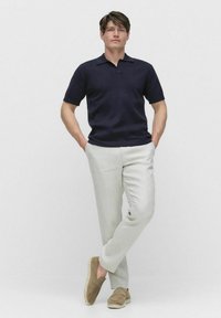 Mörkblå kortärmad polo, ljusbeige byxor och bruna slip-in skor. Slät textur, avslappnad passform och enkel design med krage.