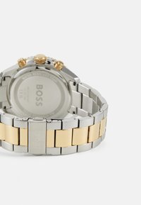 Montre en acier inoxydable argentée et dorée avec un bracelet à maillons multiples, fonctionnalités chronographe et boîtier rond. Conception résistante à l'eau.